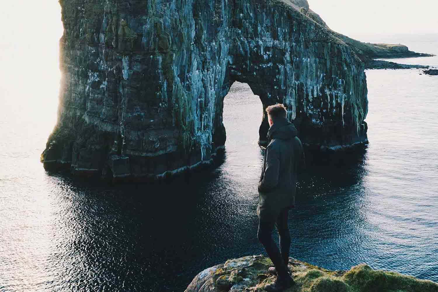 Man standing on cliff looking at rock formations in the water